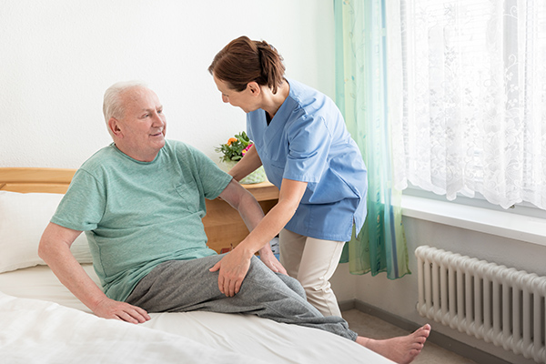 Home caregiver helping an elderly man out of bed